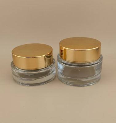 Un pot de crème de verre transparent avec un couvercle à vis dorée pour la lotion féminine